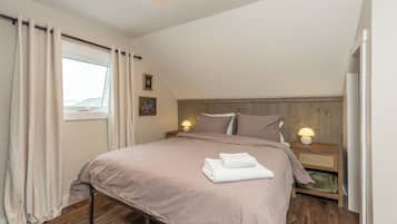 Une chambre à coucher avec un lit, deux lampes de chevet, une fenêtre avec des rideaux, une tête de lit en bois et un mur orné de deux tableaux encadrés.