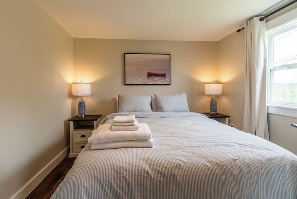 A neatly made bed with a striped bedspread and two pillows, flanked by nightstands with lamps. A framed picture of a boat on water is centered above the bed.