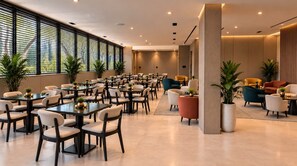 A modern hotel lobby with multiple dining tables and chairs, potted plants, and a seating area with sofas and armchairs. - Lev Hotel (Buenos Aires)