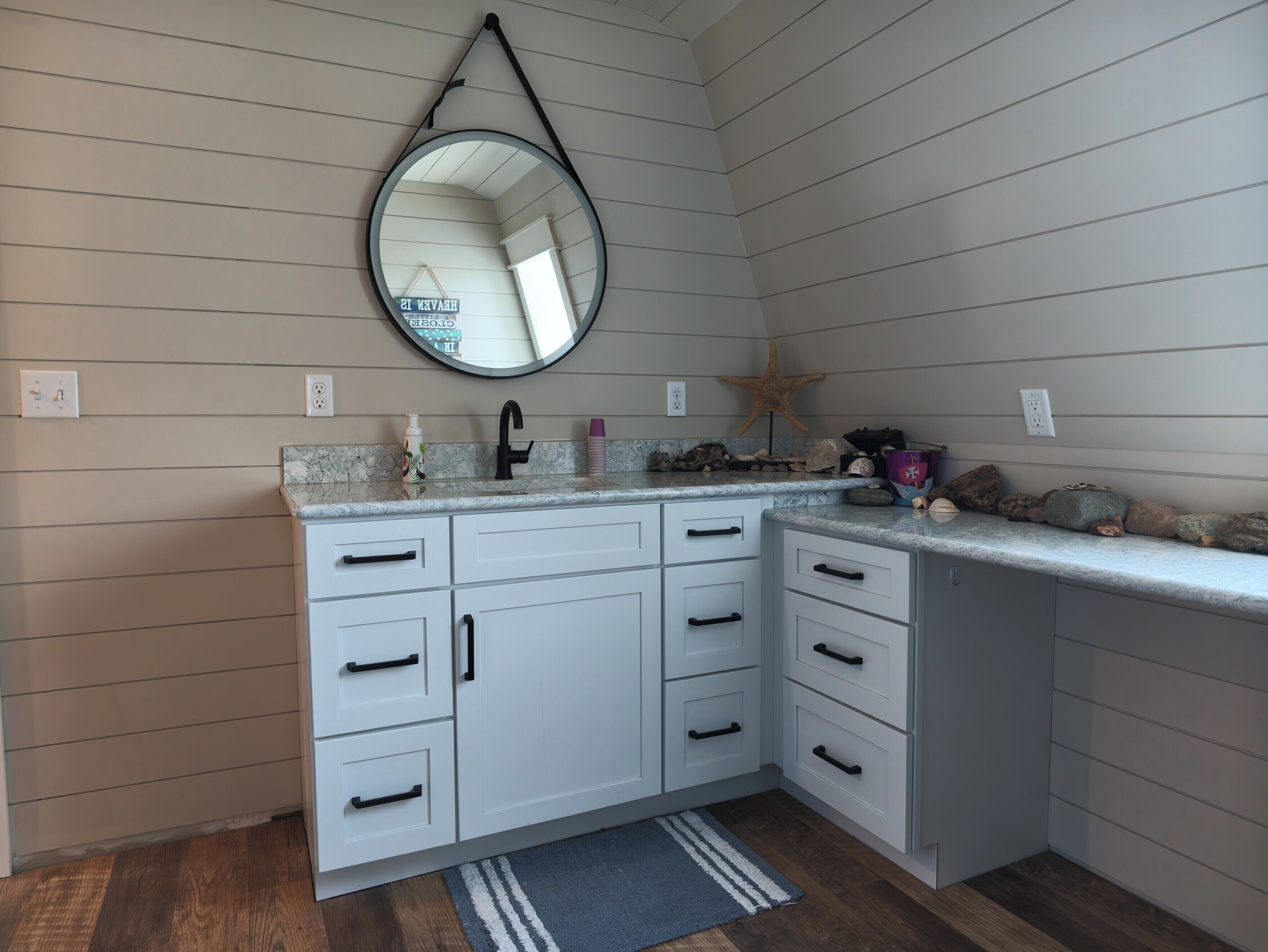 Un baño con tocador blanco, espejo redondo, grifo negro y decoración con una estrella de mar.