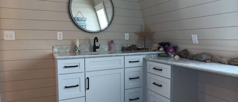 Un baño con tocador blanco, espejo redondo, grifo negro y decoración con una estrella de mar.