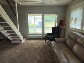 A room with a staircase, a leather sofa, a chair, and a window with a view of the outdoors. - Glass-Front Lake Cottage, Fire Pit, Sleeps 7. Wireless internet, Heat/AC. (Horton)