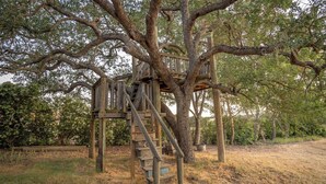 Uma casa na árvore de madeira com uma escada construída no tronco, em um ambiente natural.