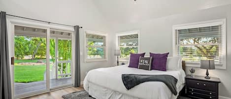 A bedroom with a large bed, two bedside tables, a chandelier, and a view of a garden through the sliding glass door.