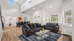Uma sala de estar ampla com um sofá grande, uma mesa de centro de vidro e uma área de jantar com mesa e cadeiras.