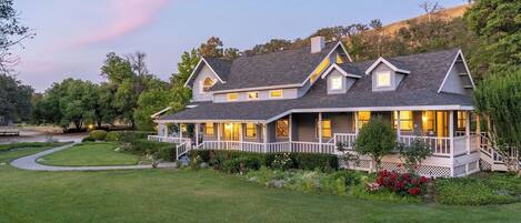 A two-story house with a wrap-around porch, a well-maintained lawn, and a variety of flowering plants.