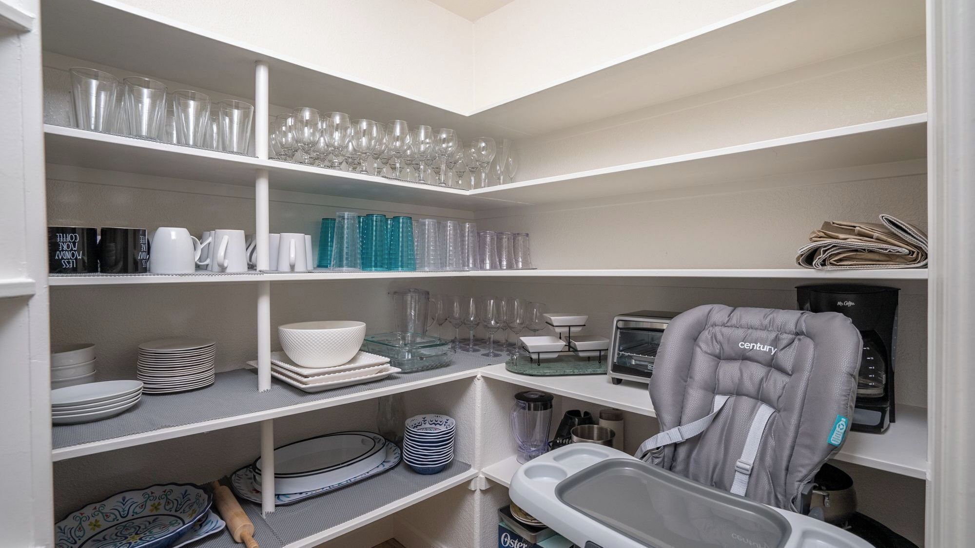 A kitchen with white shelves holding various glassware, plates, and a coffee machine.