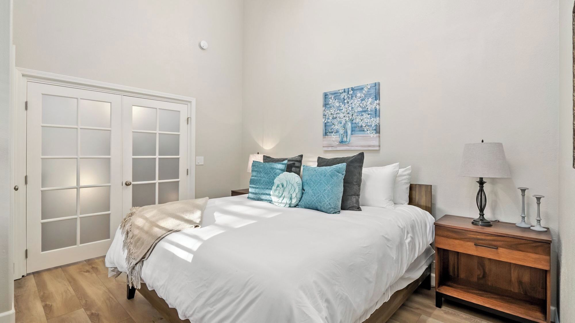 A bedroom with a bed, bedside table, lamp, and a painting on the wall.