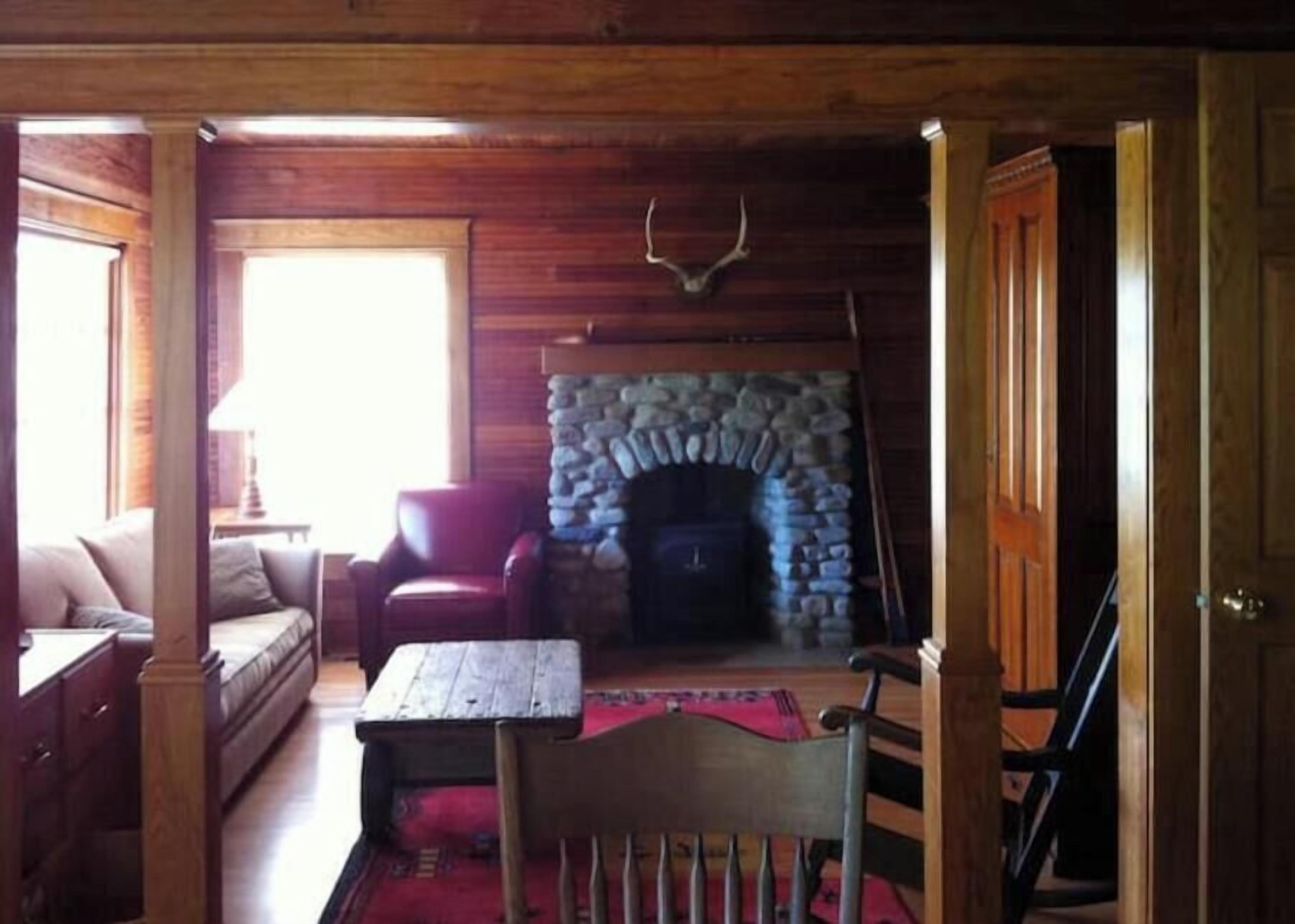 A cozy room with a stone fireplace, wooden furniture, and a view of the outdoors.