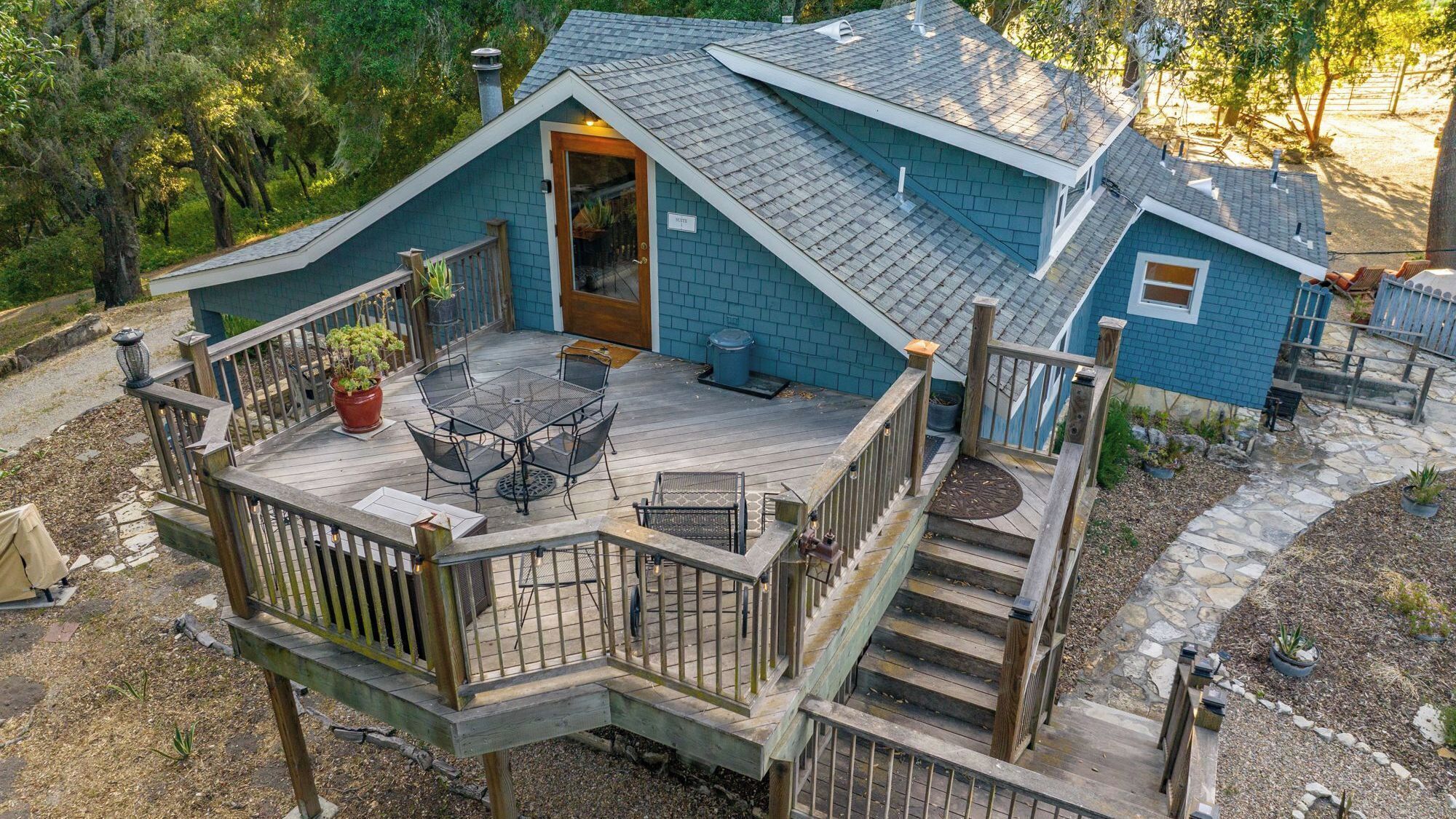 A two-story house with a deck, a covered outdoor seating area, and a staircase leading to the upper level.