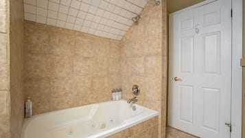 Um banheiro com banheira, uma porta branca e paredes revestidas de azulejos bege.
