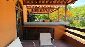 Ein Balkon mit zwei weißen Stühlen, einem kleinen Tisch und einer Holz-Pergola.