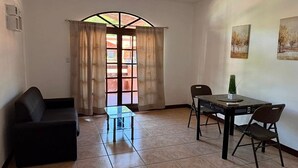 Ein Zimmer mit einer Couch, einem Esstisch mit Stühlen, einem Glastisch und einem Fenster mit Vorhängen.
