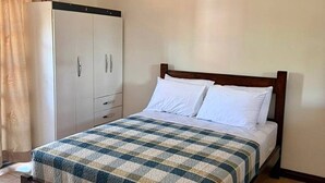 Ein Einzelbett mit karierter Bettdecke, einem Holz-Kopfteil und weißen Kissen.