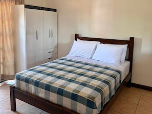 Uma cama de solteiro com colcha xadrez, cabeceira de madeira e travesseiros brancos.