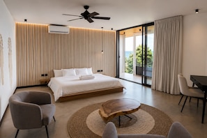 A modern hotel room with a large bed, a ceiling fan, a dining table, and a view of the outdoors. - Seataya Palace - 3-BDR Ocean View Luxury Villa & Infinity Pool (Santa Teresa)