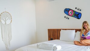 Ein modernes Schlafzimmer mit einem Holzbett, weißer Bettwäsche, einem Deckenventilator, einer Klimaanlage, einem Traumfänger und einem Skateboard an der Wand.