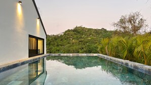 Ein moderner Pool mit klarem Wasser, umgeben von üppiger Vegetation und einer Hügelkuppe.