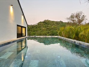 Ein moderner Pool mit klarem Wasser, umgeben von üppiger Vegetation und einer Hügelkuppe.