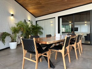 Ein moderner Essbereich mit Holztisch und -stühlen, Topfpflanzen und Blick ins Freie durch große Fenster.