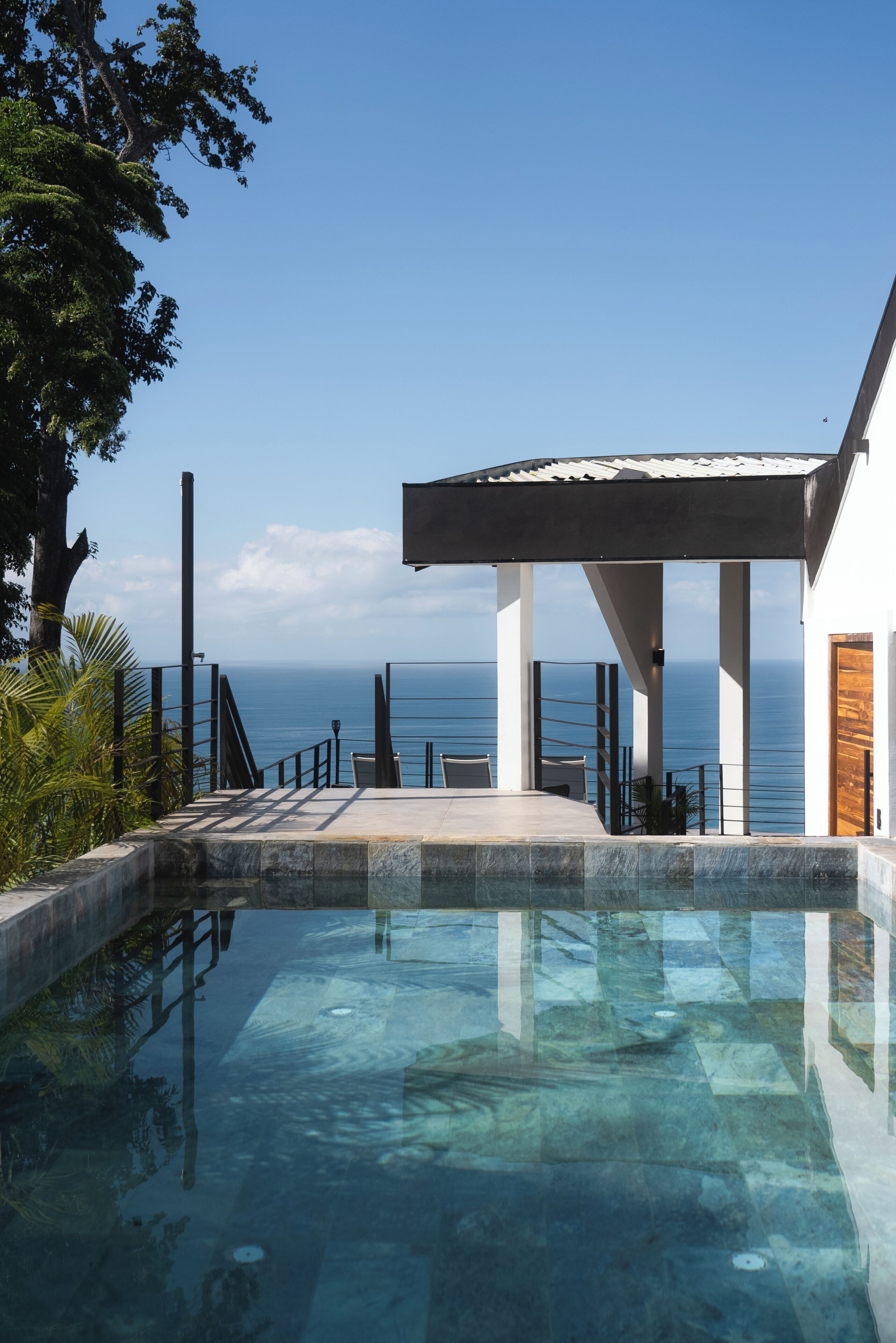 A modern pool area with clear water, a covered seating area, and a view of the ocean.