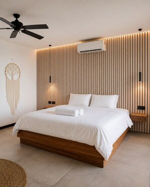 Une chambre à coucher moderne, équipée d’un lit, d’un ventilateur de plafond, d’un climatiseur et d’un attrape-rêves fixé au mur.