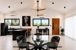 A modern kitchen with a central island, black chairs, and a dining table with a glass top. - Seataya Palace - 3-BDR Ocean View Luxury Villa & Infinity Pool (Santa Teresa)
