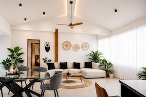 A modern living room with a white sofa, a dining table, and chairs. There is a ceiling fan, a coffee table, and decorative wall art. - Seataya Palace - 3-BDR Ocean View Luxury Villa & Infinity Pool (Santa Teresa)