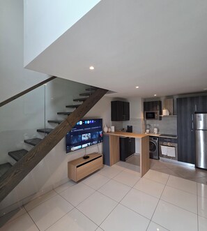 A modern kitchen with a built-in TV, a wooden staircase, and a dining area. - Cozy 1-BEDROOM EBS PROPERTIES L (Accra)