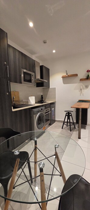 A compact kitchen with modern appliances, a glass dining table, and a small seating area. - Cozy 1-BEDROOM EBS PROPERTIES L (Accra)