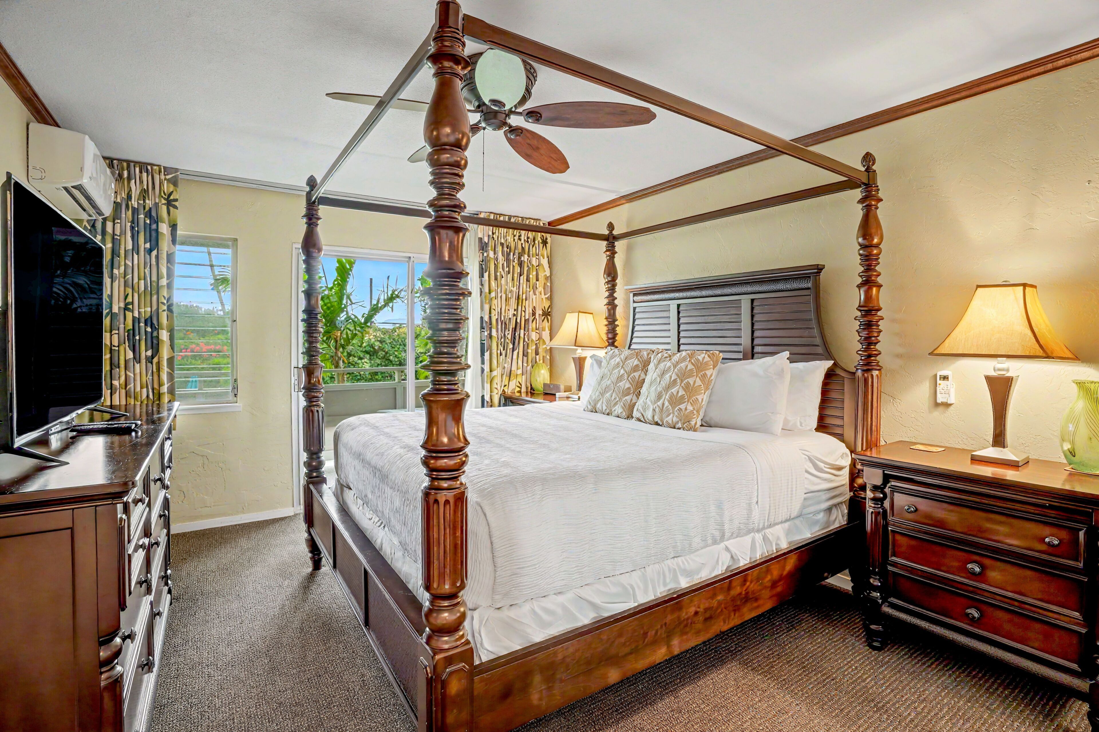 A four-poster bed with a ceiling fan, a television, and a nightstand with a lamp.