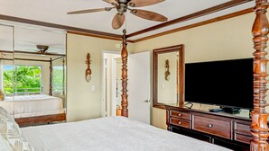 A bedroom with a bed, a television, and a ceiling fan.