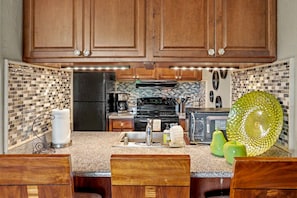 Une cuisine avec des meubles de rangement en bois, un réfrigérateur noir, un four à micro-ondes, une cuisinière et un évier.