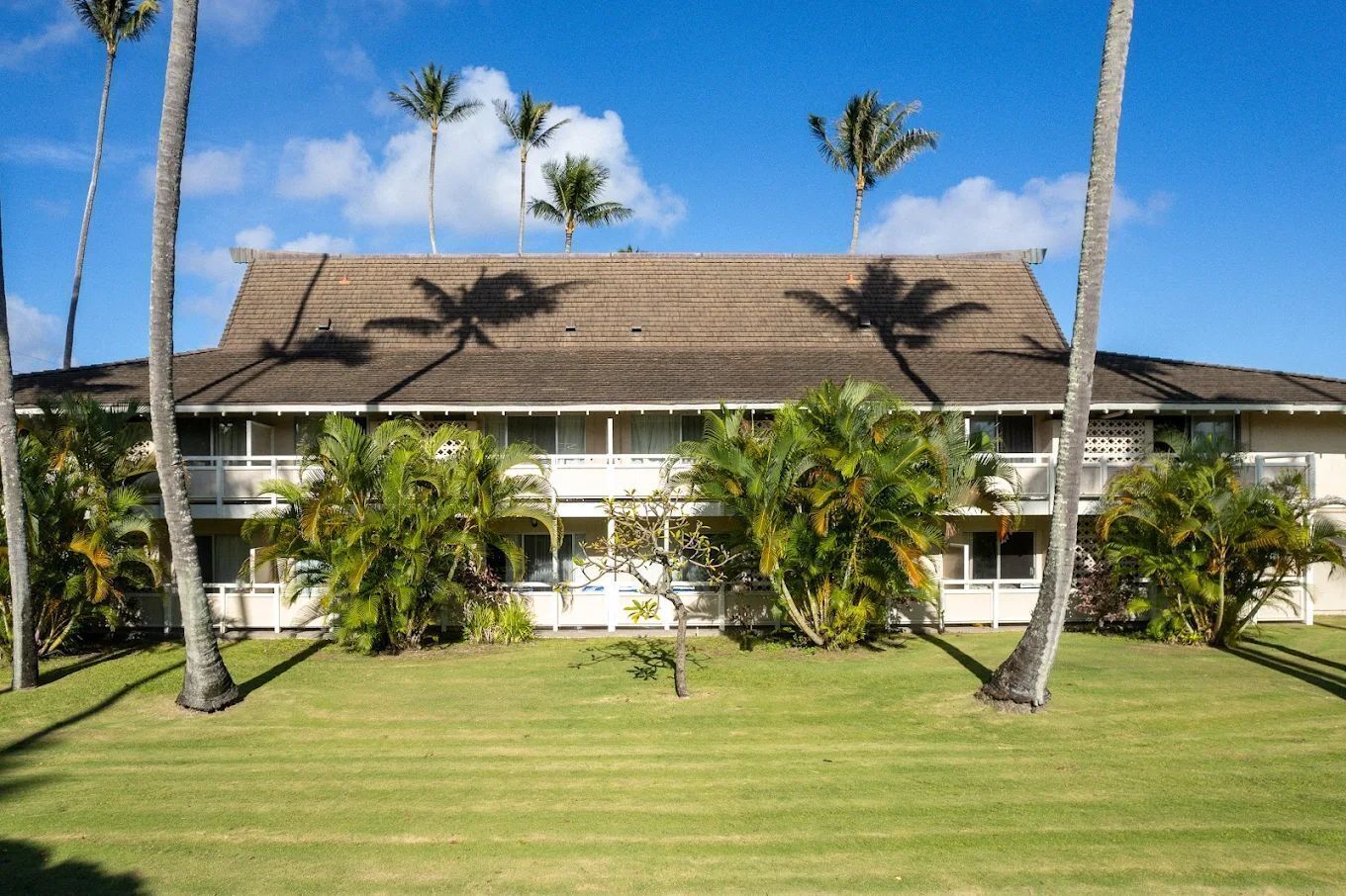 A two-story hotel with a flat roof, surrounded by palm trees and a well-maintained lawn.