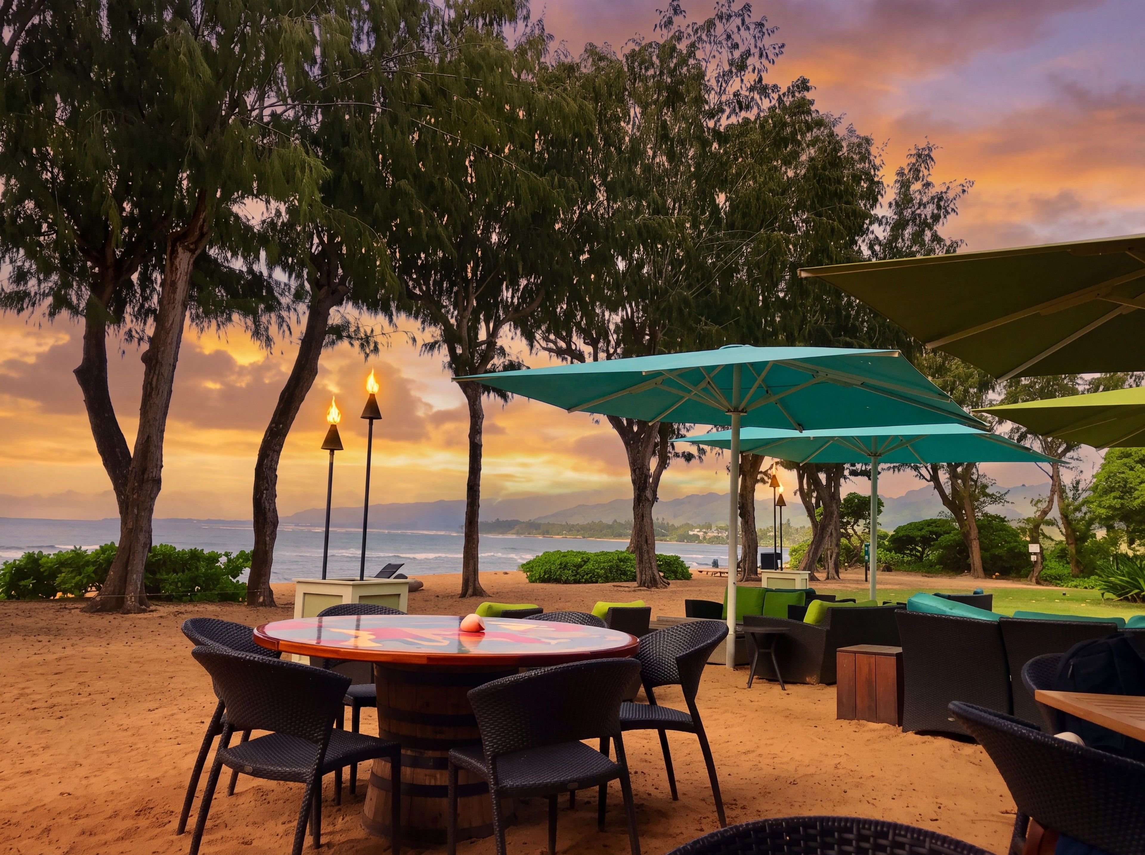 A beachside outdoor seating area with a round table and chairs, surrounded by trees and overlooking the sea.