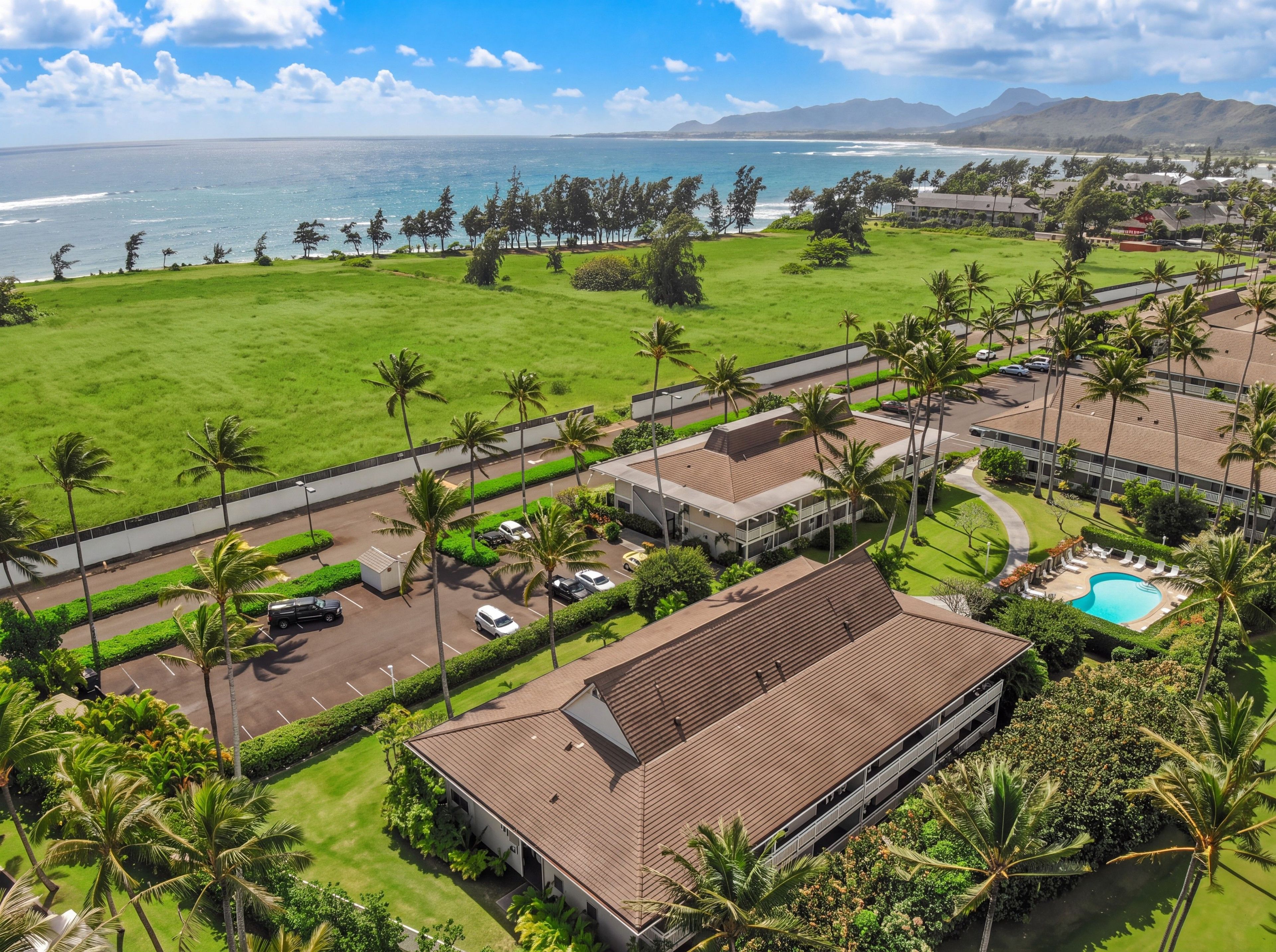 A resort with a swimming pool, a parking area, and a view of the ocean.