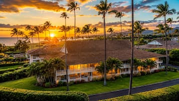 A beachfront property with a large house, palm trees, and a view of the ocean at sunset.