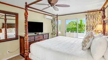 A four-poster bed with a ceiling fan, a television on a dresser, and a view of greenery through the window.