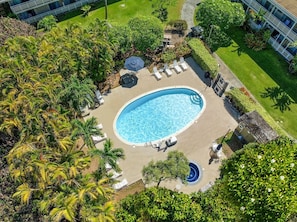 Vue aérienne d’un complexe hôtelier doté d’une piscine centrale, de chaises longues et d’un aménagement paysager de style tropical.