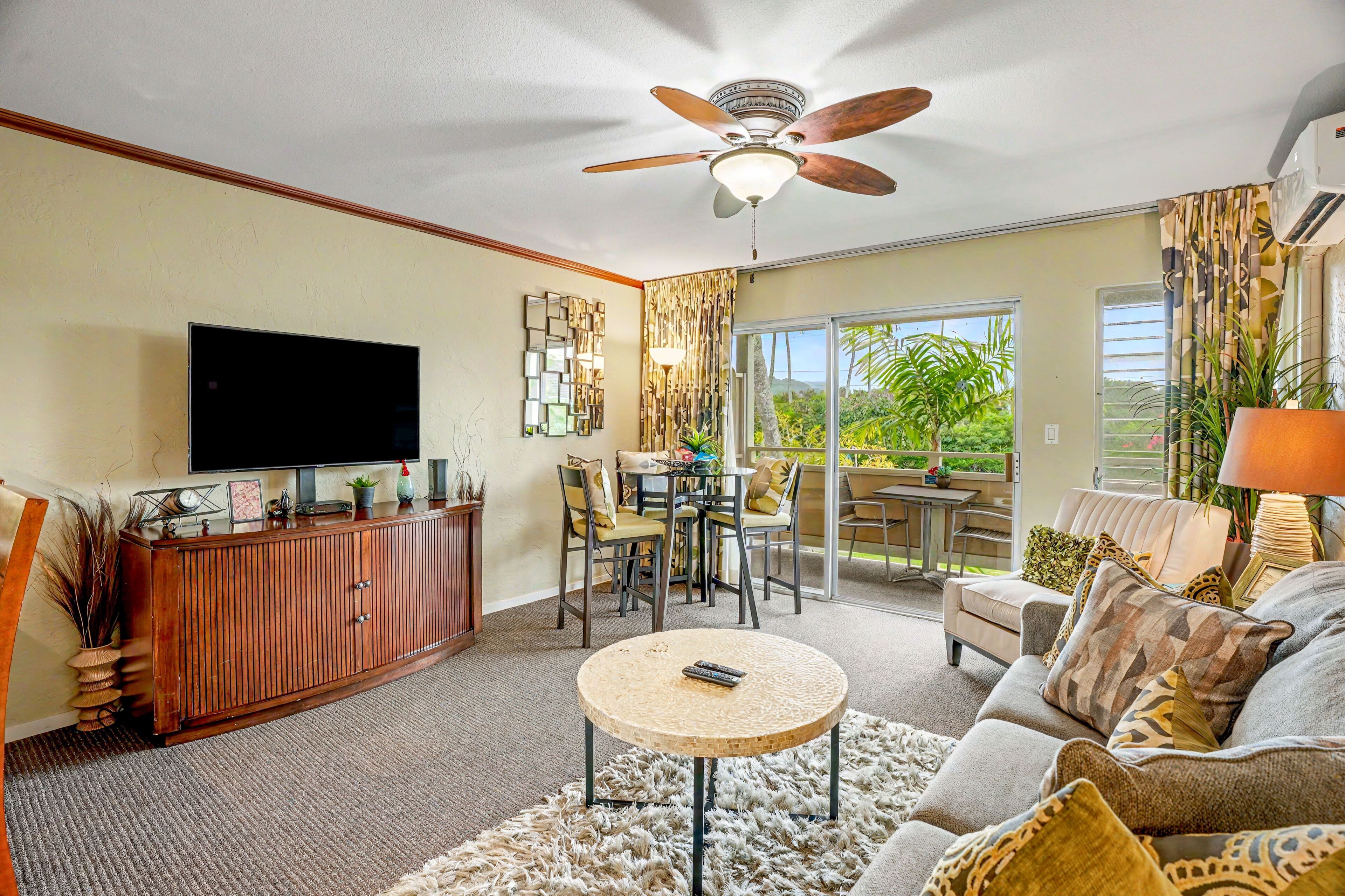 A living room with a flat-screen TV, wooden entertainment unit, and a ceiling fan.
