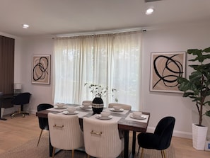A dining area with a table set for four, chairs, a vase with greenery, and abstract art on the walls.