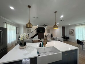 A modern kitchen with a central island, pendant lighting, and a staircase leading to a living area.