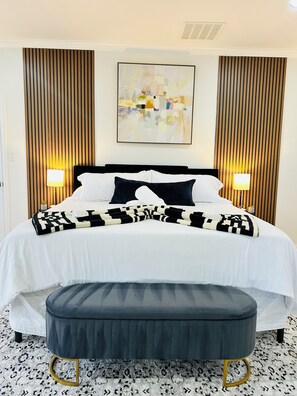 Ein Hotelzimmer mit einem Bett, Nachttischlampen, einem an der Wand hängenden abstrakten Gemälde und einem gemusterten Teppich.