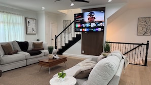 Ein modernes Wohnzimmer mit Flachbildfernseher, einer Couch, einem Couchtisch und einer Treppe.
