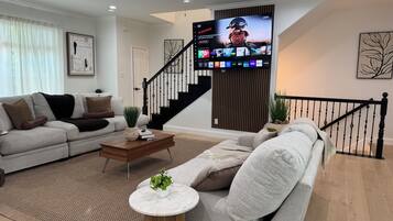 A modern living room with a flat-screen TV, a sofa, a coffee table, and a staircase.