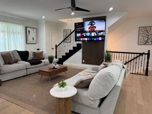 Una sala de estar moderna con una televisión de pantalla plana, un sofá, una mesa de centro y una escalera.