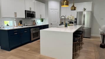 A modern kitchen with white cabinetry, a central island, stainless steel appliances, and pendant lighting.