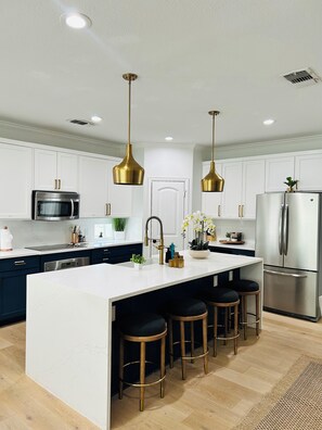 A modern kitchen with a central island, stainless steel appliances, and gold pendant lighting.