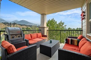 A covered patio with wicker furniture, a barbecue grill, and a view of mountains.