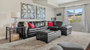 Ein modernes Wohnzimmer mit einer schwarzen Ledersofa, einem Couchtisch und Blick auf Berge durch ein großes Fenster.